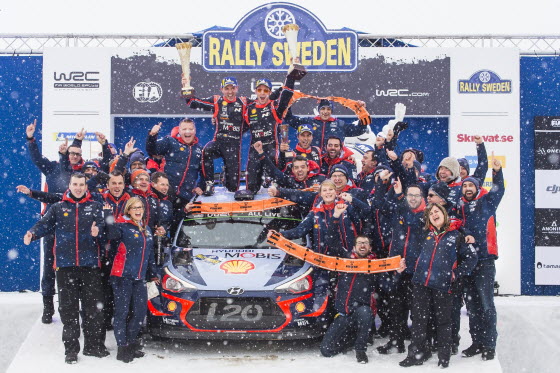 2018 WRC 스웨덴 랠리에서 시상대에서 현대 월드랠리팀 선수 및 관계자들의 기념사진. 신형 i20 랠리카 위에서 니콜라스 질술(Nicolas Gilsoul, 왼쪽)과 티에리 누빌(Thierry Neuville)이 우승컵을 들고 환호하는 모습.ⓒ현대차