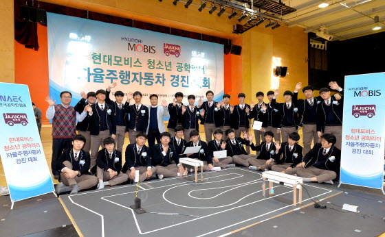 인천 하늘고등학교에서 개최된 ‘현대모비스 청소년 공학리더 자율주행차 경진대회’에 참가한 아이들이 모형 도로 앞에서 손을 들어 보이고 있다.ⓒ현대모비스