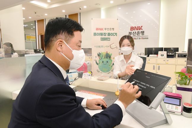 BNK부산은행이 환경보호 및 ESG 경영 실천을 위해 고객과 직원이 함께하는 종이통장 줄이기 '지금(紙禁), 나부터' 이벤트를 시행한다.ⓒBNK부산은행