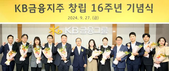 KB금융지주는 27일 KB국민은행 신관에서 임직원 60여 명이 참석한 가운데 창립 16주년 기념식을 가졌다고 밝혔다. 사진은 KB금융그룹 양종희 회장(왼쪽 여섯 번째)이 창립 16주년 기념식에서 장기근속직원들과 기념 촬영을 하는 모습. [KB금융그룹 제공.]